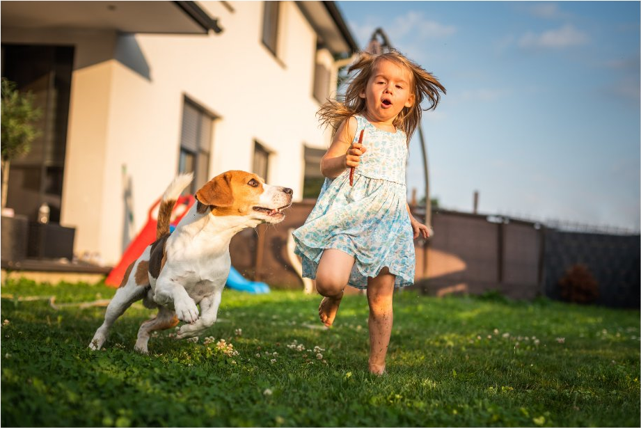 A child running barefoot in a clean backyard with the family dog
